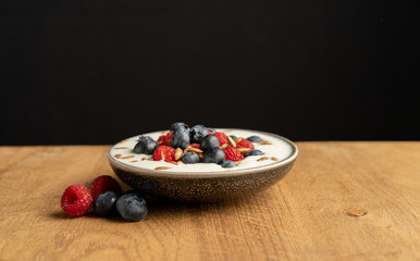 Tasty fresh blueberry raspberries  yoghurt shake dessert in ceramic bowl standing on black dark table background.