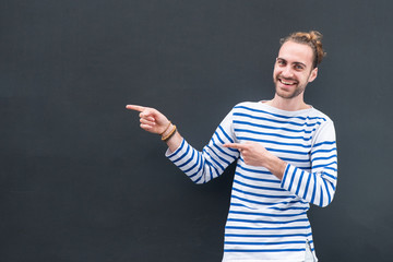 happy young man with beard pointing fingers to empty space on black background