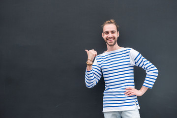 happy young man with beard pointing thumb to empty space on black background