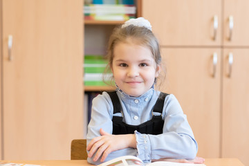 Girl schoolgirl sits at a desk with books, and smiles.