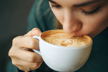 Close up girl is drinking coffee. She enjoys her morning cappuccino or flat white. - obrazy, fototapety, plakaty