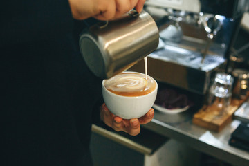Barista pours milk or cream into coffee and draws a drawing on the foam.