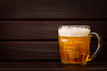 Beer pouring into a glass, with foam, on wooden table. Free copy space