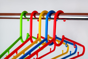 Close-up of multicolored plastic clothes hangers on a rod in the closet. Set of new colorful...