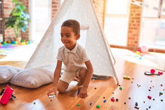Beautiful african american toddler playing with cars around lots of toys at kindergarten