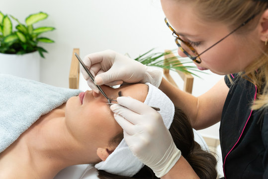 Twarz kobiety podczas zabiegu przyklejania rzęs. Stylistka rzęs wykonuje zabieg metodą objętościową. Przedłużanie rzęs w salonie kosmetycznym. 