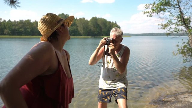 Elderly man taking picture of attractive senior woman with vintage camera on the beach. Funny active loving elderly couple carefree and happy together on vacation in Northern Europe, Finland