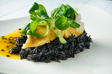 Grilled pike perch with garlic garnished with black rice and mango sauce on a white plate on a...