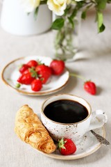 Breakfast. Croissant and strawberry. And black coffee, a bouquet of flowers. Fresh strawberries. 