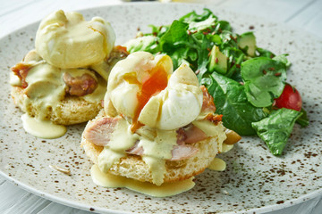 Breakfast with toasts with creamy garlic sauce, bacon and poached eggs with lettuce on a ceramic plate on a white wooden background