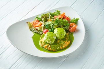 Breakfast with poached eggs with lettuce, salmon and mashed potatoes on a ceramic plate on a white wooden background. Close up on tasty food