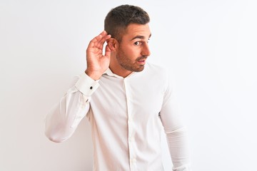 Young handsome business man wearing elegant shirt over isolated background smiling with hand over ear listening an hearing to rumor or gossip. Deafness concept.