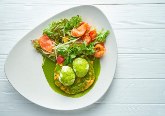 Breakfast with poached eggs with lettuce, salmon and mashed potatoes on a ceramic plate on a white wooden background. Close up on tasty food