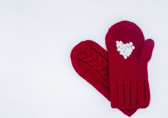 Two knitted red mittens lie on top of each other, one of them has white snowflakes in the shape of a heart on a white background, isolated. Concept of Christmas, winter, love and St. Valentine's day.