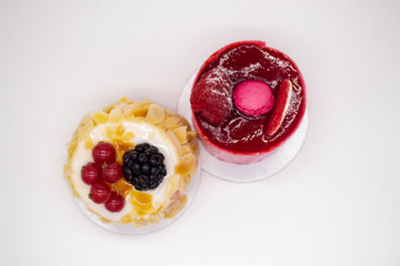 Two cakes on a white background: Bright red with raspberries, berry jelly, macaroon on top and cream cake with almond petals, red currants and blackberries. Concept of holiday, birthday, sweet tooth