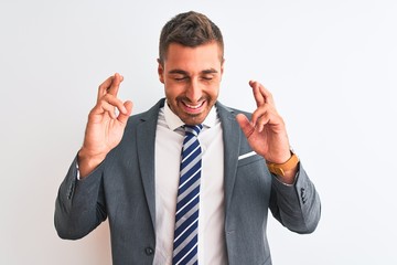 Young handsome business man wearing suit and tie over isolated background gesturing finger crossed smiling with hope and eyes closed. Luck and superstitious concept.