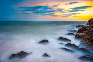 Long exposure of the sea during a golden sunset with waves crashing around the jetty