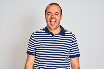 Fototapeta premium Young man wearing casual striped polo standing over isolated white background sticking tongue out happy with funny expression. Emotion concept.