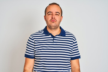 Fototapeta premium Young man wearing casual striped polo standing over isolated white background looking at the camera blowing a kiss on air being lovely and sexy. Love expression.