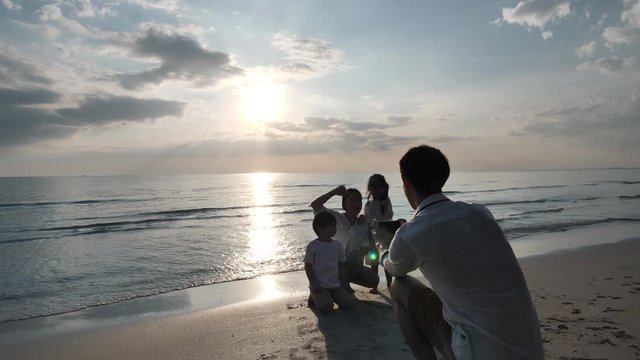 Happy Asian Family On Summer Vacation Father takes family photos with smartphone on the beach. Relax Holiday and Travel concept. Slow motion