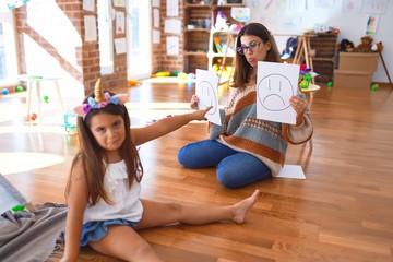 Beautiful pshychologist and toddler doing therapy with emotions emoji around lots of toys at kindergarten