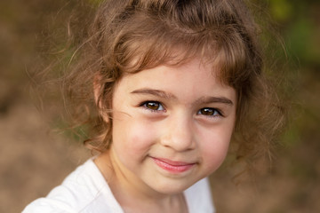 Portrait of smiling beautiful little girl at green of summer park.Cute child looking at the camera