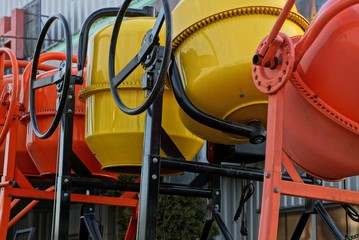 row of new iron red and yellow concrete mixers on the street against the wall