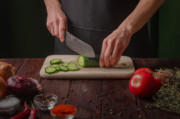 Beautiful female hands cut a fresh cucumber on a wooden board. Cooking light diet food. Homemade...