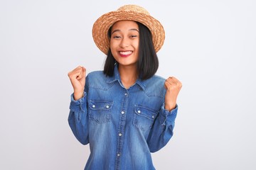 Obraz na płótnie Canvas Young beautiful chinese woman wearing denim shirt and hat over isolated white background celebrating surprised and amazed for success with arms raised and open eyes. Winner concept.