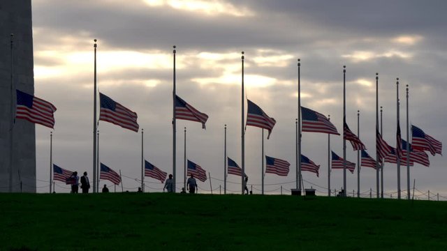 Gorgeous shot of American flags at half-mast at base of Washington monument at sunset