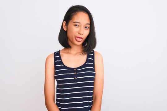 Young chinese woman wearing striped t-shirt standing over isolated white background sticking tongue out happy with funny expression. Emotion concept.
