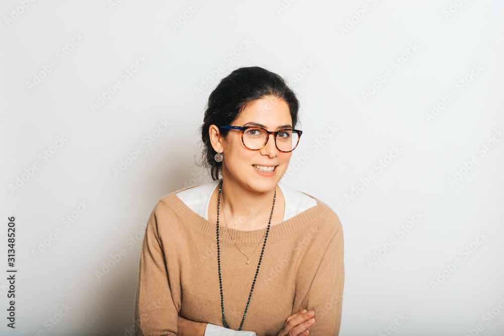 Wall mural Studio portrait of beautiful brunette woman, wearing glasses, arms crossed, posing on white background