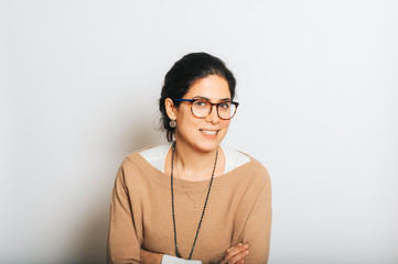 Studio portrait of beautiful brunette woman, wearing glasses, arms crossed, posing on white...