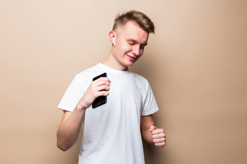 Portrait of a happy man using mobile phone, celebrating standing isolated over beige background