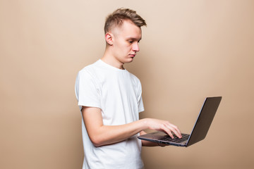 Portrait if a happy man dressed standing with on laptop computer isolated over beige background,