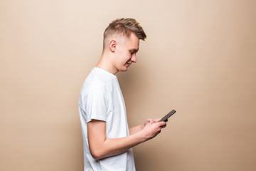 Young casual man holding mobile phone isolated over beige background