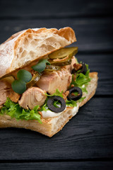 American fast food. Juicy tuna sandwich with cheese, salad and olives on a dark background. Club food.