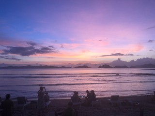 Fototapeta premium Silhouettes of people on a beach watching purple sunset on the vacation 