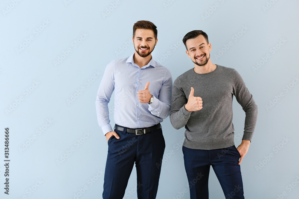 Wall mural Portrait of young businessmen showing thumb-up gesture on color background