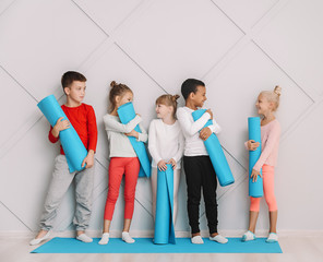Little children with yoga mats near grey wall in gym
