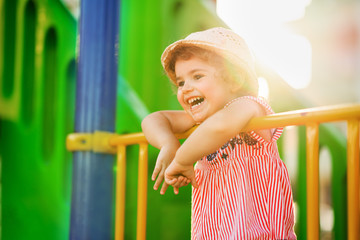 Little cute girl playing in playground an wearing hat. Concept play in outdoors in summer time.