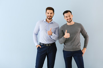 Portrait of young businessmen showing thumb-up gesture on color background