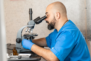 Male laboratory assistant examining biomaterial samples in a microscope