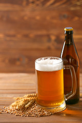 Bottle and mug of tasty beer on wooden background