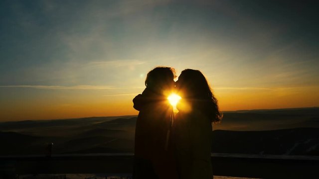 couple in love kisses standing on snowy slope at back sunset