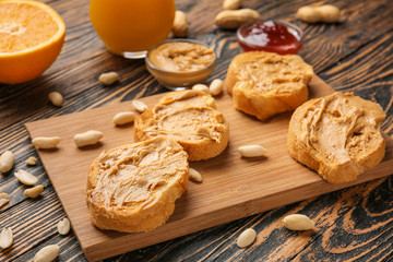 Board with fresh bread and tasty peanut butter on wooden table