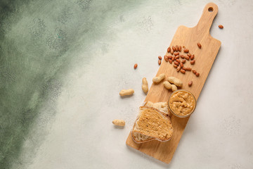 Board with fresh bread and tasty peanut butter on light background