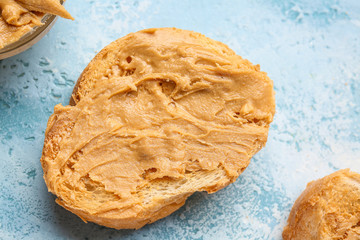 Slice of bread with tasty peanut butter on color background