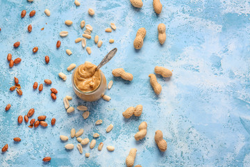 Tasty peanut butter in jar on color background