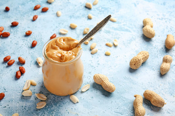 Tasty peanut butter in jar on color background
